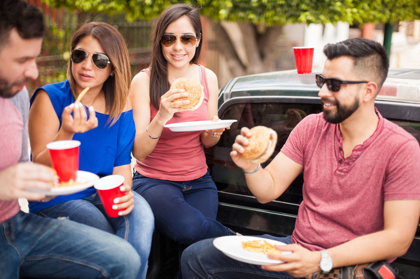 Two young couples wearing sunglasses and eating burgers on a pick up truck on a sunny day in summer