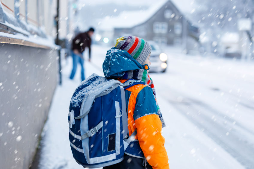 young school boy bundled up waiting outside for school bus