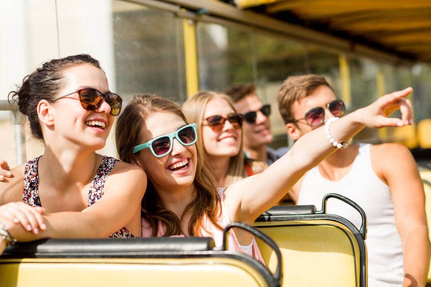 group of smiling friends traveling by bus to a concert