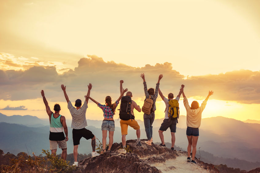 Group of happy coworkers stand with raised arms at sunset mountain and enjoys sunset