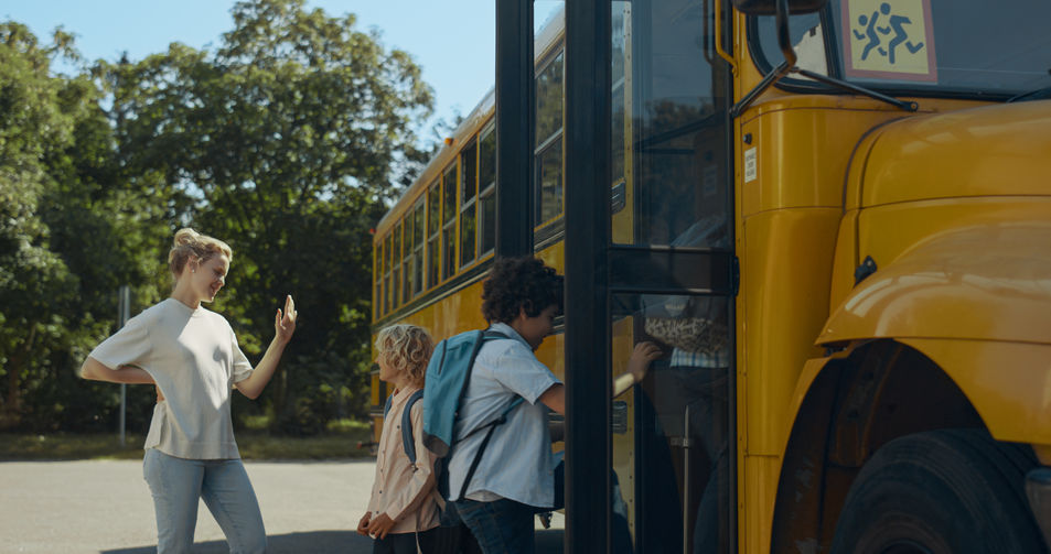 Smiling mother standing with son giving high five near school bus stop