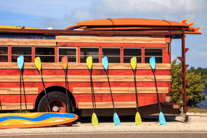 Colorful kayak and paddleboard paddles leaning against a woody bus for spring break trip